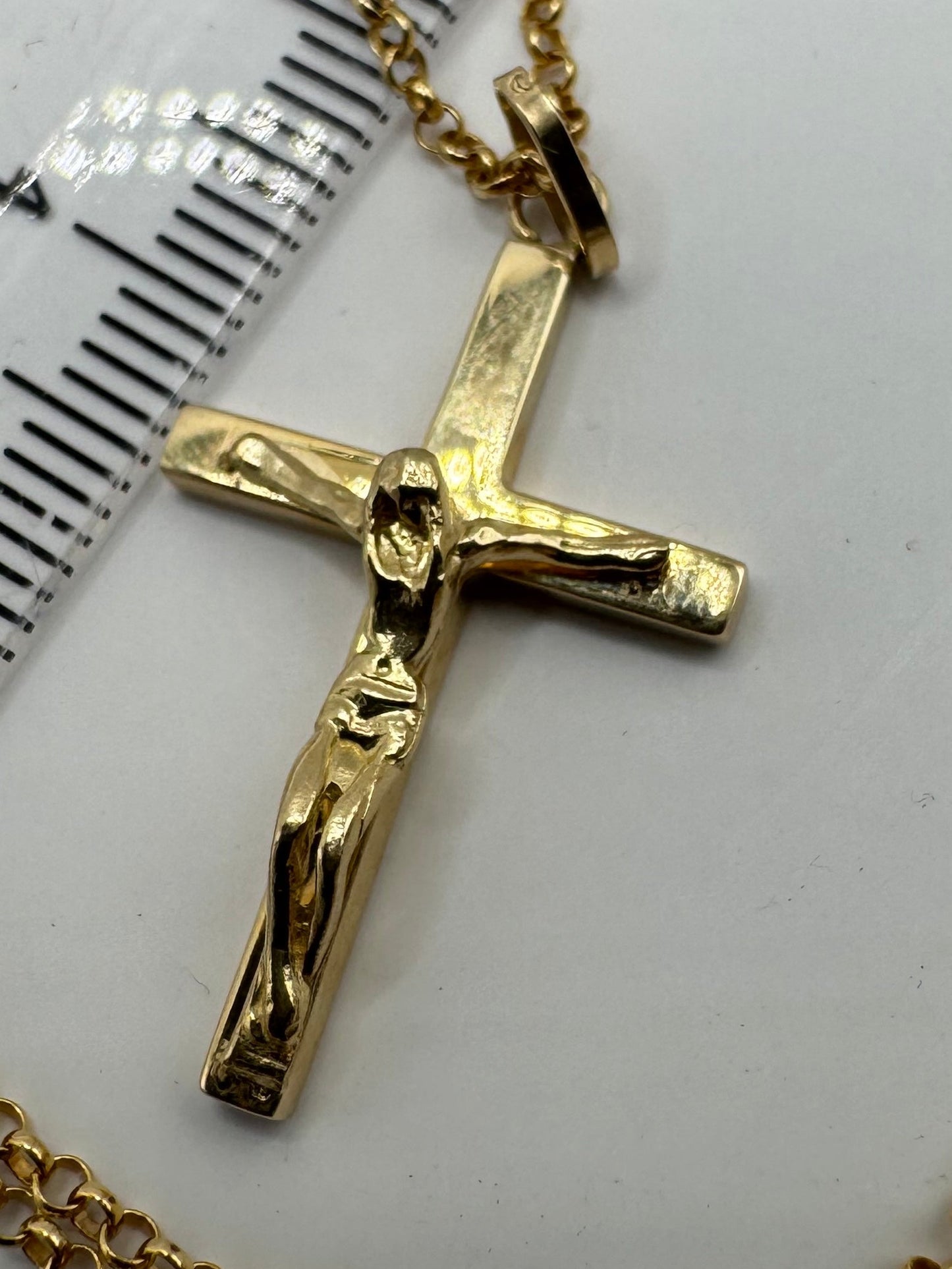 Gold crucifix pendant on a white background with a ruler for scale.