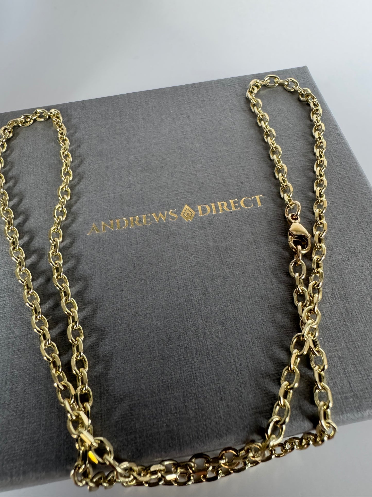 Gold chain necklace on a gray box with 'Andrews Direct' branding
