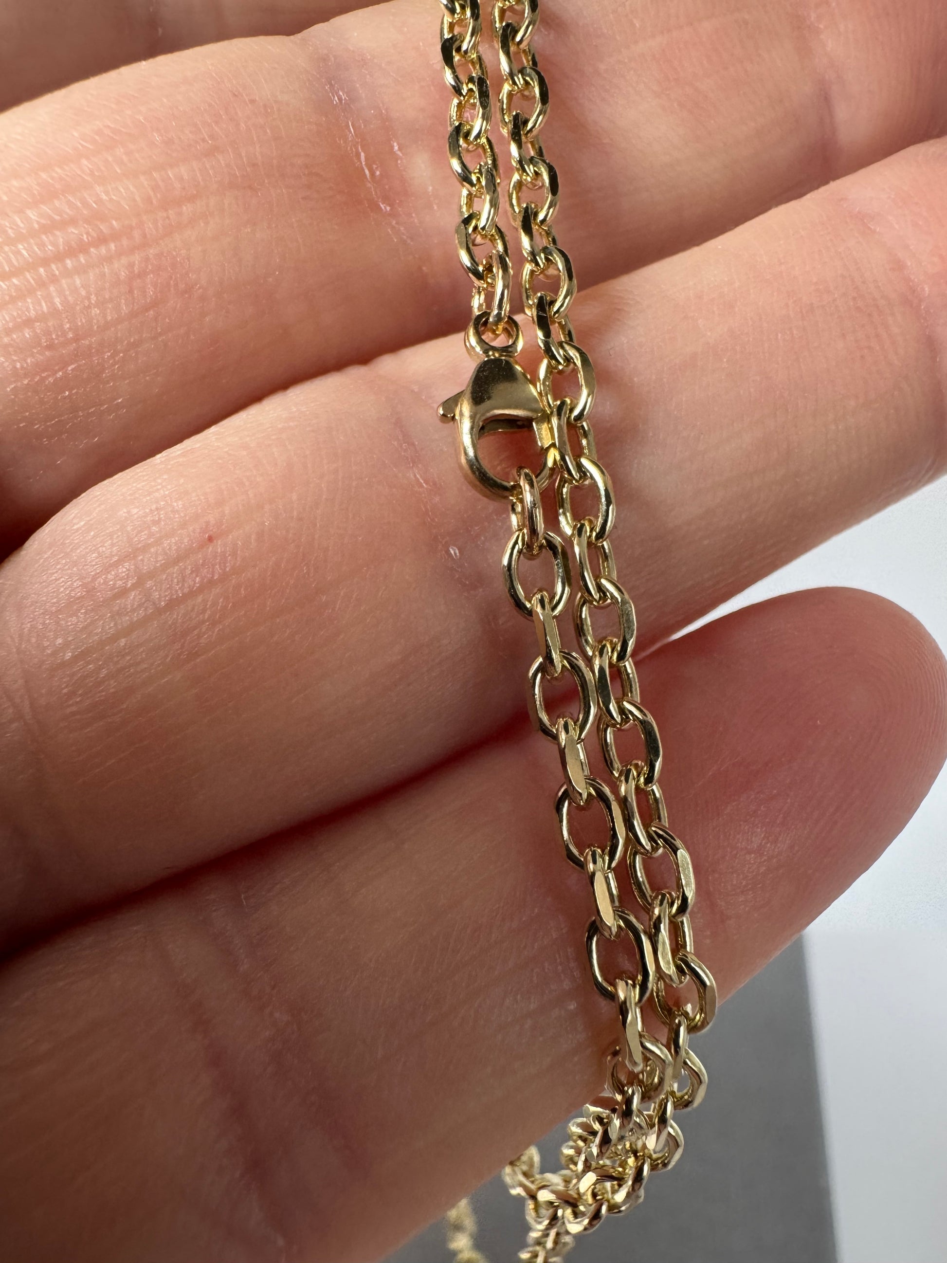 Gold chain necklace held between fingers against a neutral background
